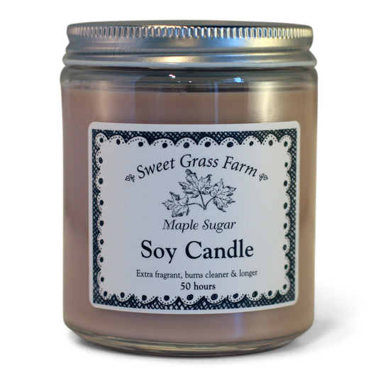 A soy wax candle in a clear glass jar with a label reading 'Sweet Grass Farm Maple Sugar Soy Candle', with a definition stating 'Extra fragrant, burns cleaner & longer 50 hours'.