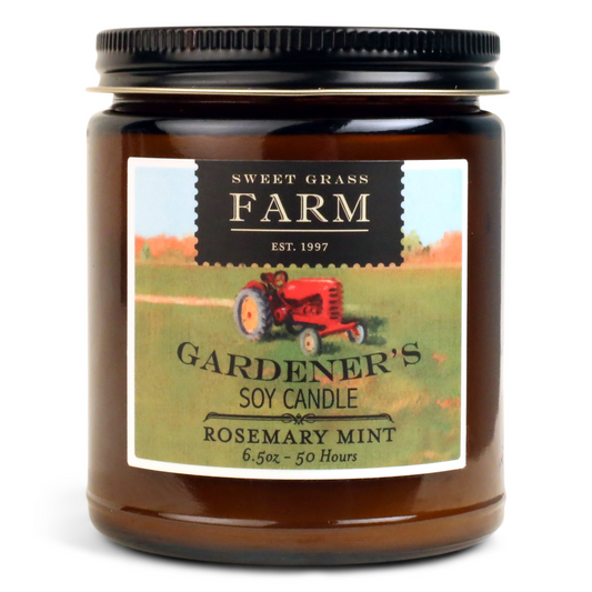 A jar candle with a label that includes a red tractor and text, indicating the brand 'SWEET GRASS FARM' and the product name 'GARDENER'S SOY CANDLE ROSEMARY MINT'. The jar is transparent and is made of glass.
