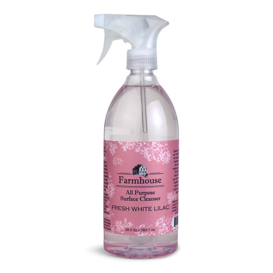 A clear spray bottle labeled 'Farmhouse' with 'All Purpose Surface Cleanser' and 'Fresh White Lilac' scent, containing a plant-based cleaner.