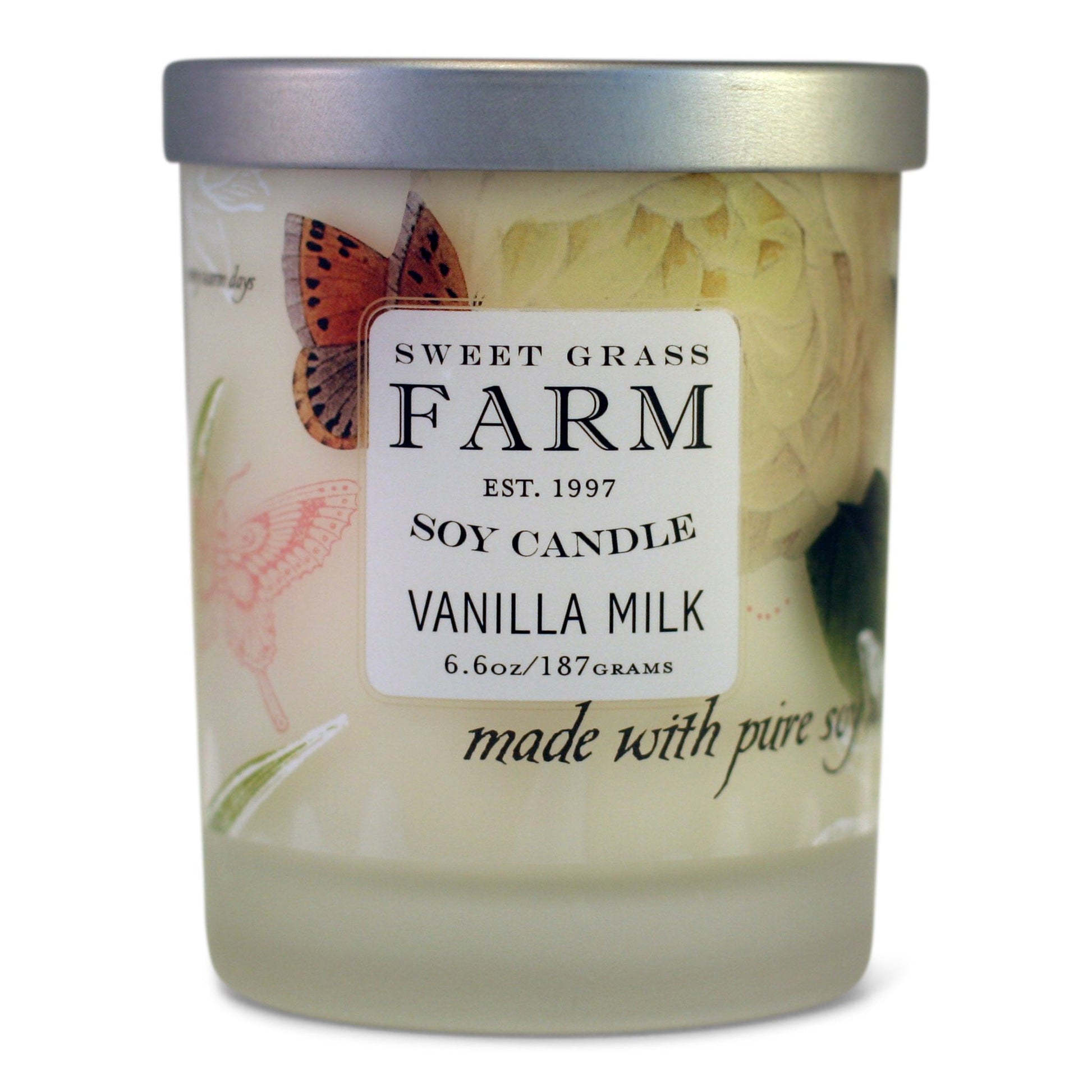 A soy wax candle in a clear tumbler with a label that reads 'Sweet Grass Farm Soy Candle, Vanilla Milk', with tan and pink botanical images in the background.