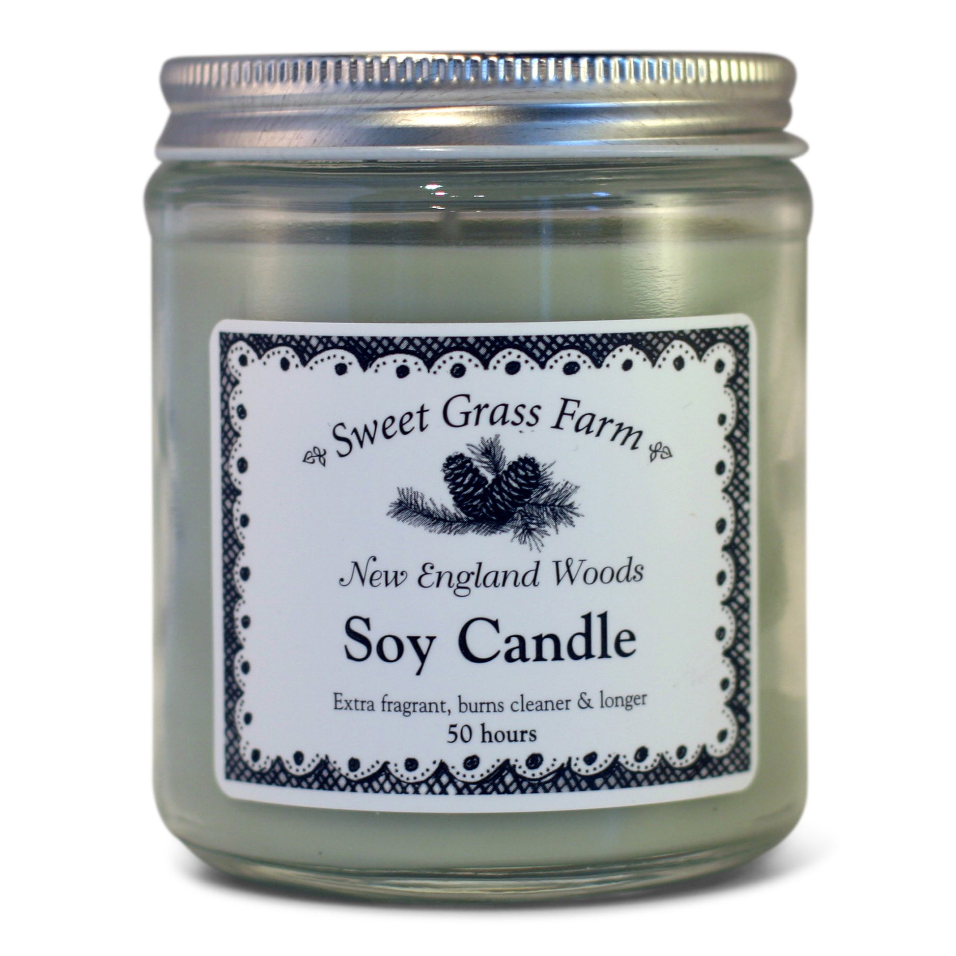 A soy wax candle in a clear glass jar with a label reading 'Sweet Grass Farm New England Woods Soy Candle', with a definition stating 'Extra fragrant, burns cleaner & longer 50 hours'.